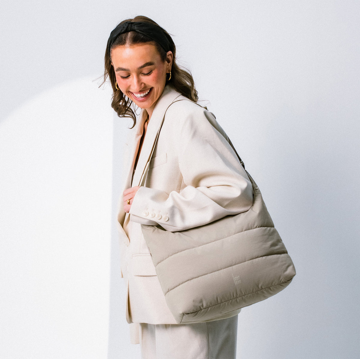 PUFFER SQUARE BAG Tasche in scallop (helles Beige) von einer lächelnden Frau über der Schulter getragen.