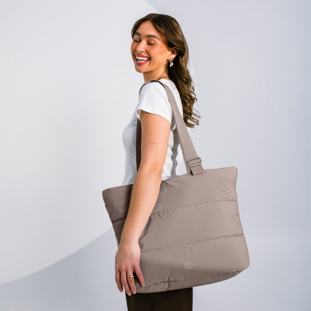 PUFFER TOTE BAG Tasche in oyster (klassisches Taupe-Braun) von einer Frau über der Schulter getragen.