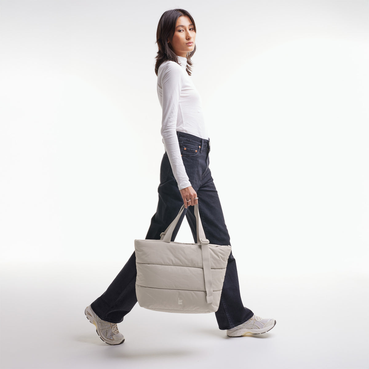 PUFFER TOTE BAG Tasche in scallop (helles Beige) von einer Frau in der Hand gehalten.
