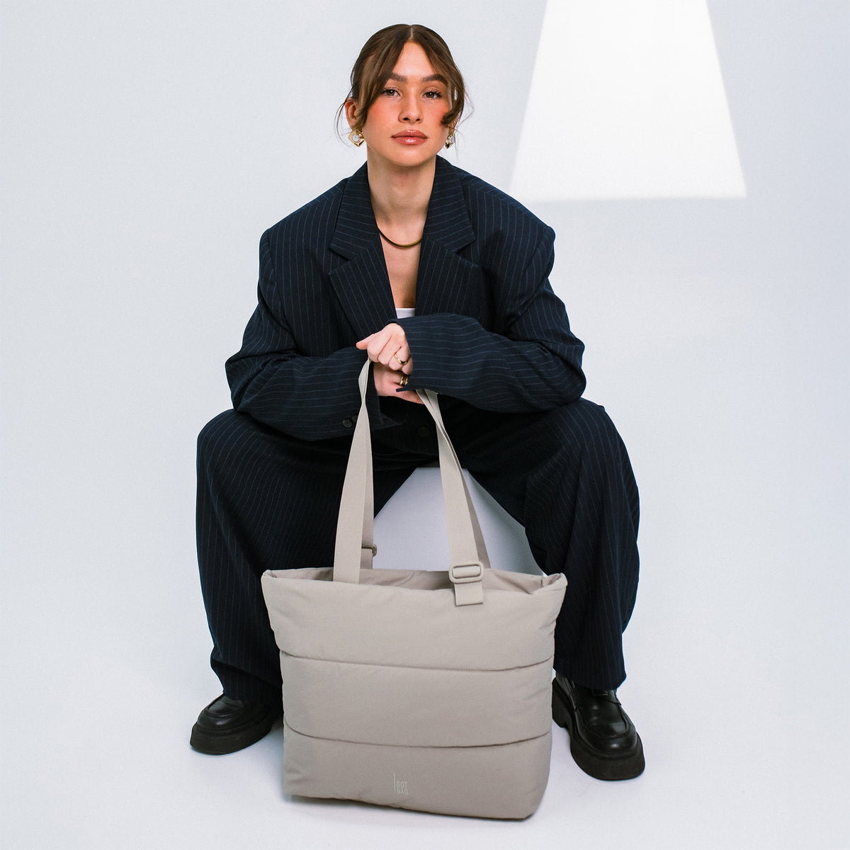 PUFFER TOTE BAG Tasche in scallop (helles Beige) von einer Frau in der Hand gehalten.