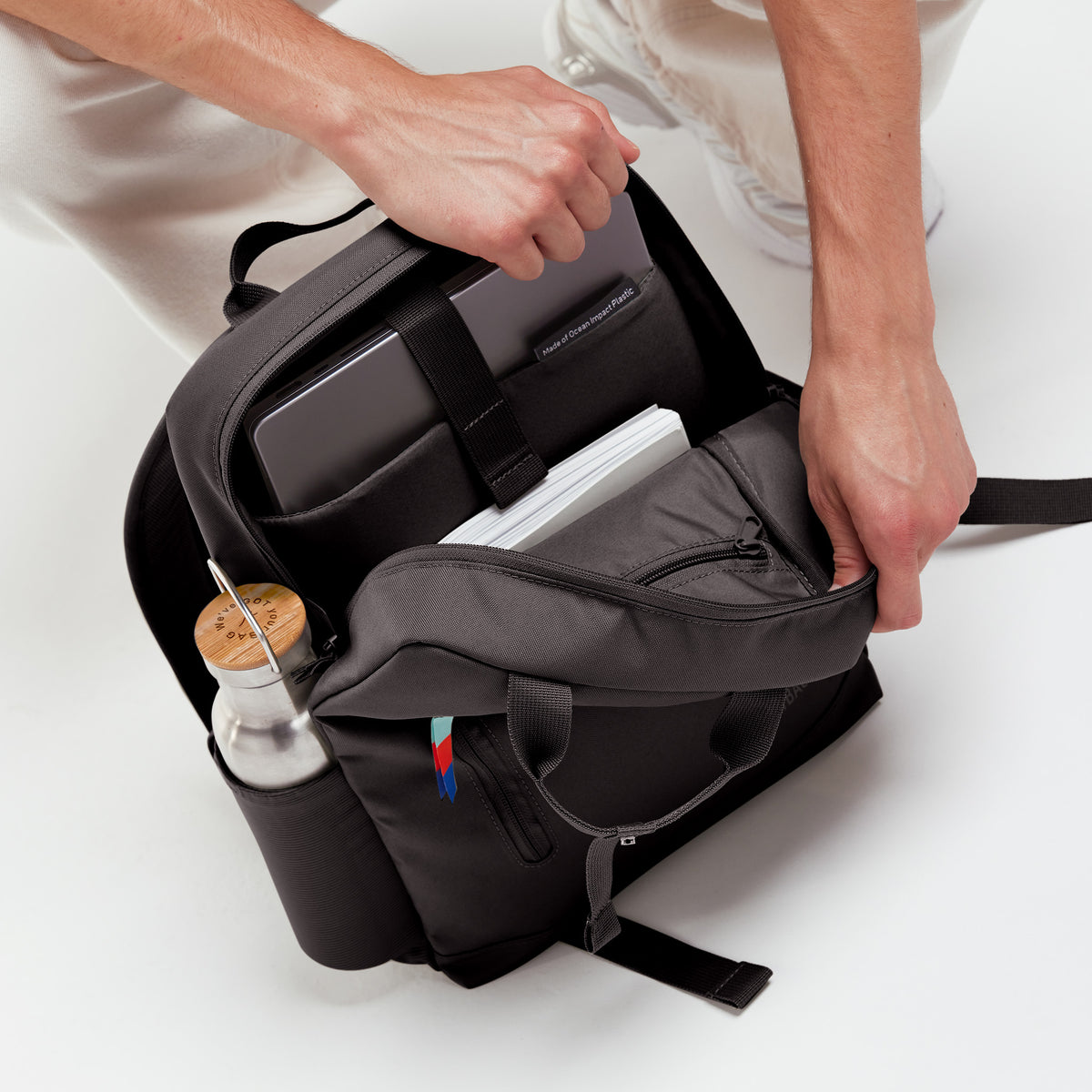 DAYPACK Rucksack in mussel (dunkles Braun-Grau) von einem Mann geöffnet, mit Laptop und Wasserflasche befüllt.