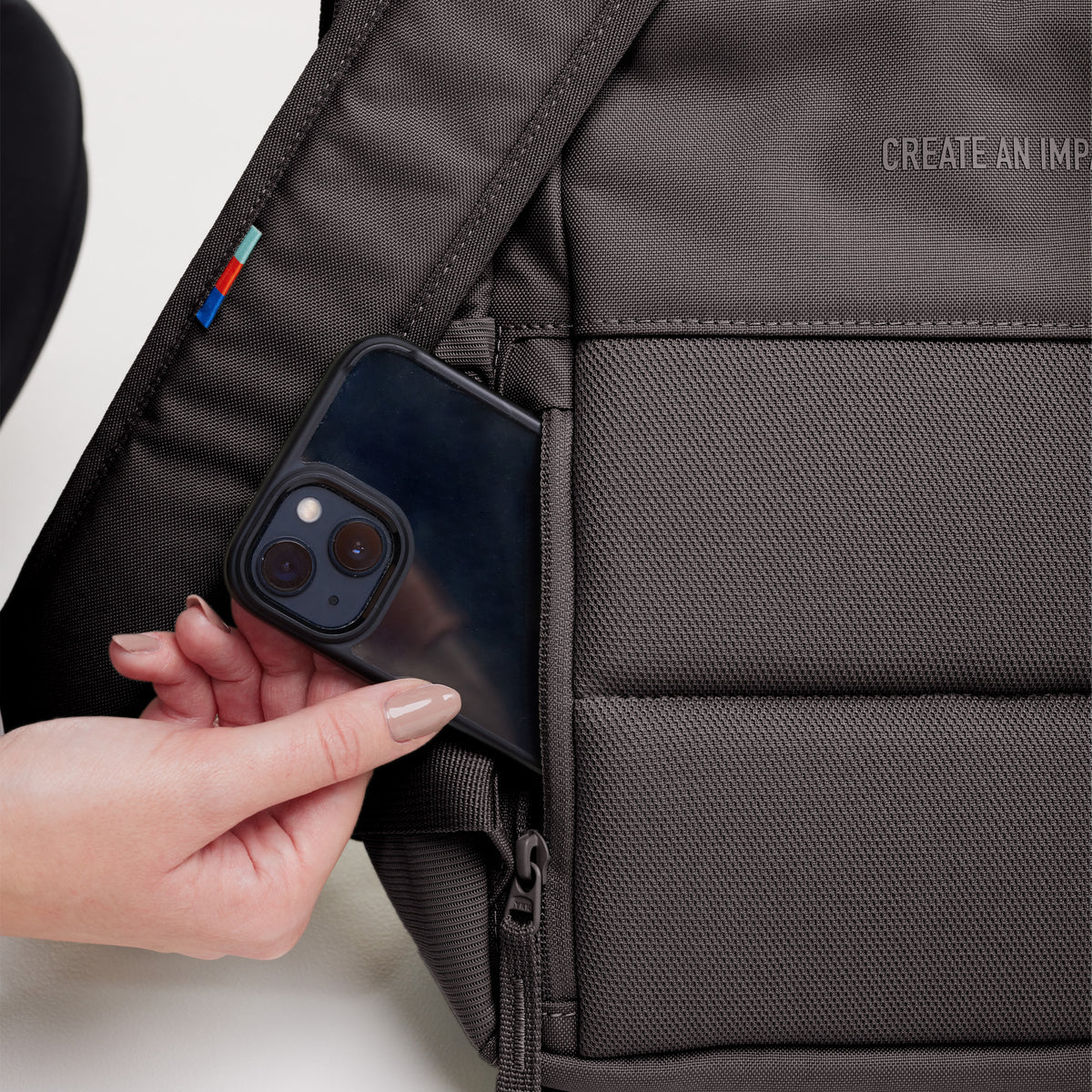DAYPACK Rucksack in mussel (dunkles Braun-Grau) von einer Frau, die ein Handy in eine Tasche steckt.