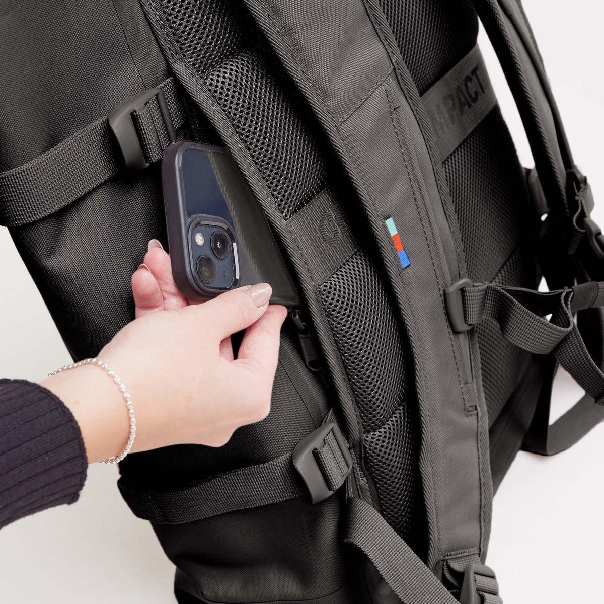 ROLLTOP Rucksack in mussel (dunkles Braun-Grau): Frau steckt Smartphone in die Seitentasche.