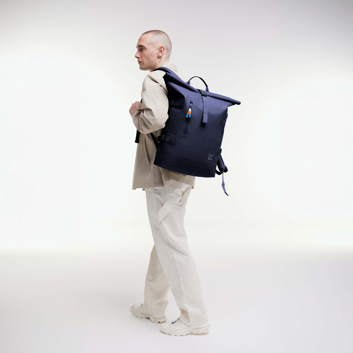 ROLLTOP Rucksack in tide (tiefes Dunkelblau mit Lilastich) von einem Mann als Rucksack auf dem Rücken getragen.
