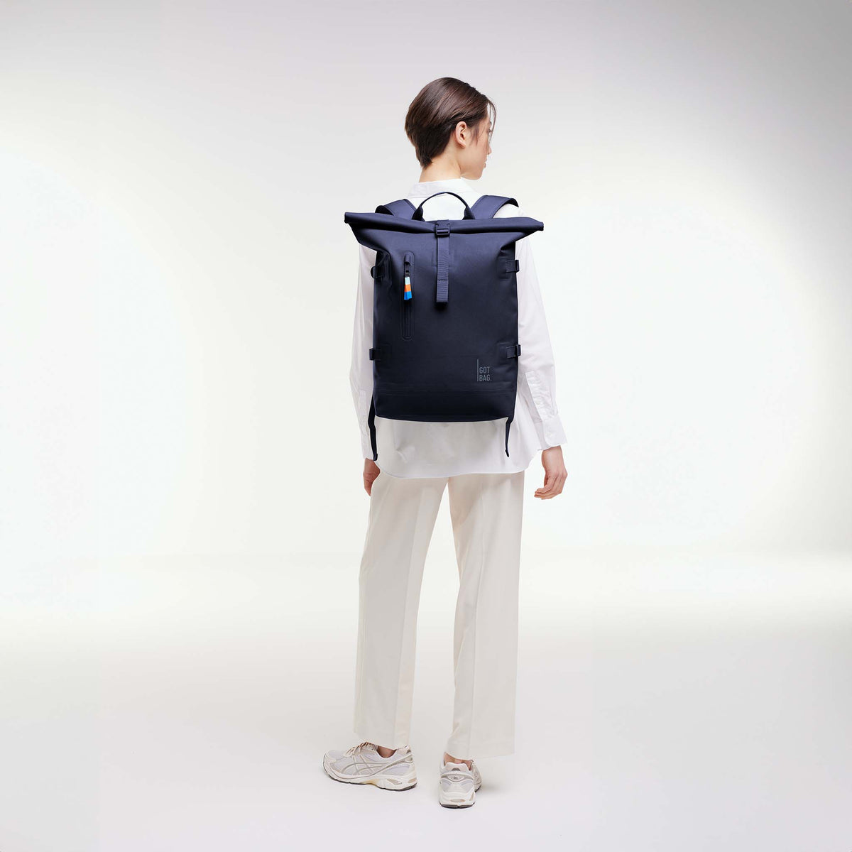 ROLLTOP Rucksack in tide (tiefes Dunkelblau mit Lilastich) von einer Frau als Rucksack auf dem Rücken getragen.