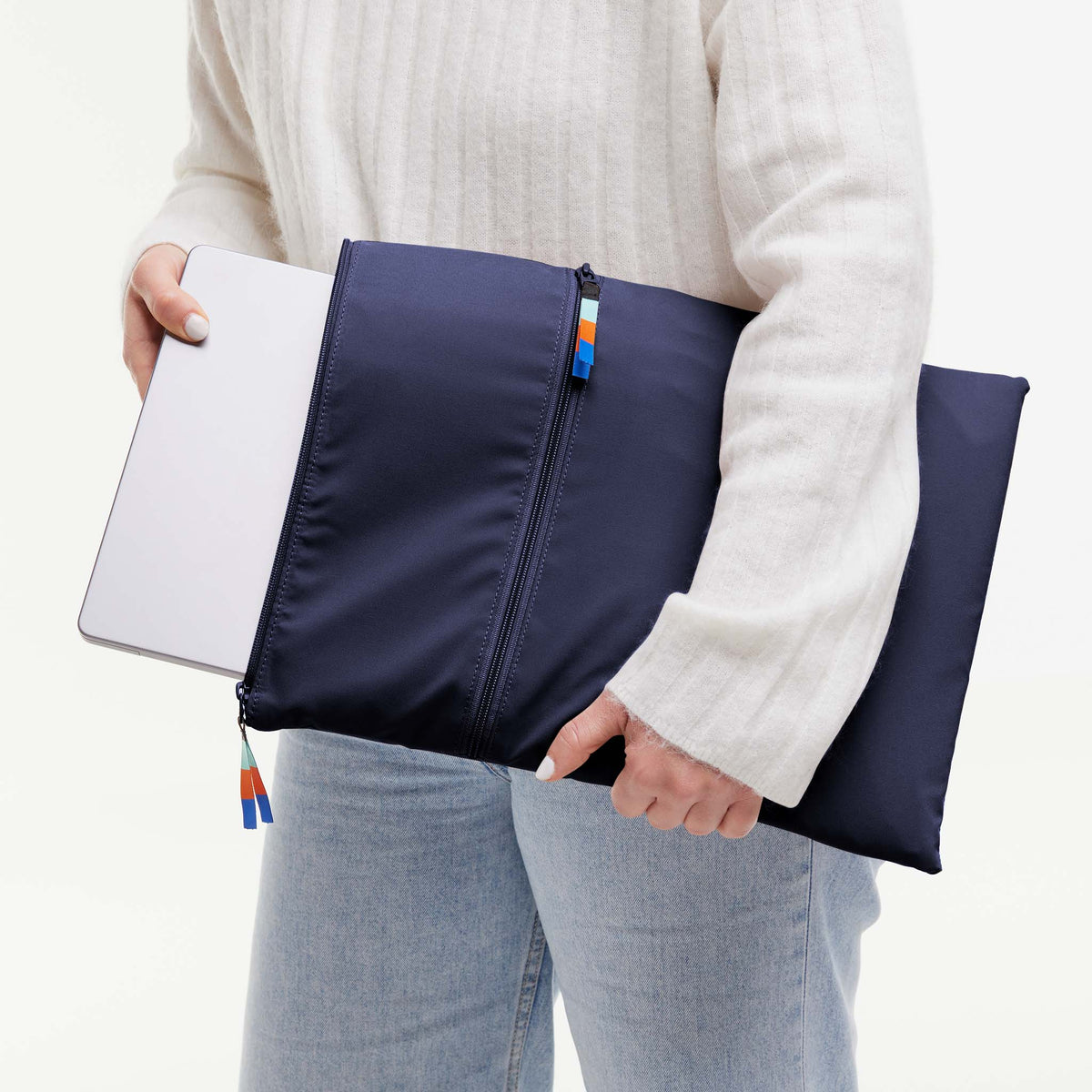 Frau verstaut Laptop in ROLLTOP 2.0 Tasche in tide (tiefes Dunkelblau mit Lilastich).