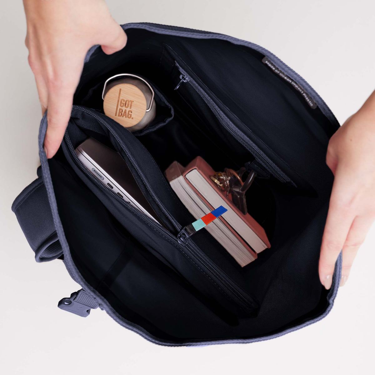 ROLLTOP Tasche in tide (tiefes Dunkelblau mit Lilastich) von Händen geöffnet, zeigt das Innere mit Fächern.