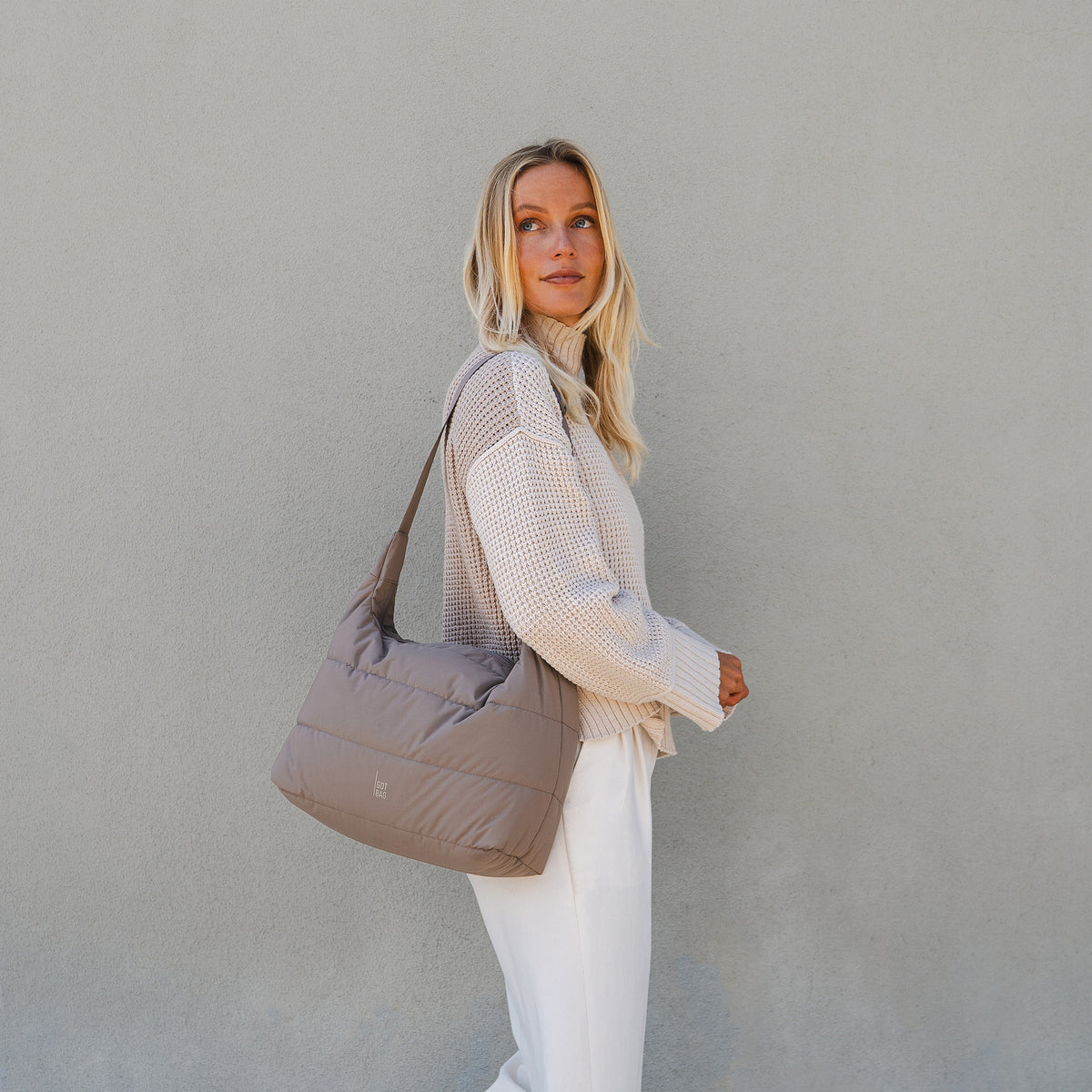 PUFFER SQUARE BAG Tasche in oyster (klassisches Taupe-Braun) von einer Frau über der Schulter getragen.