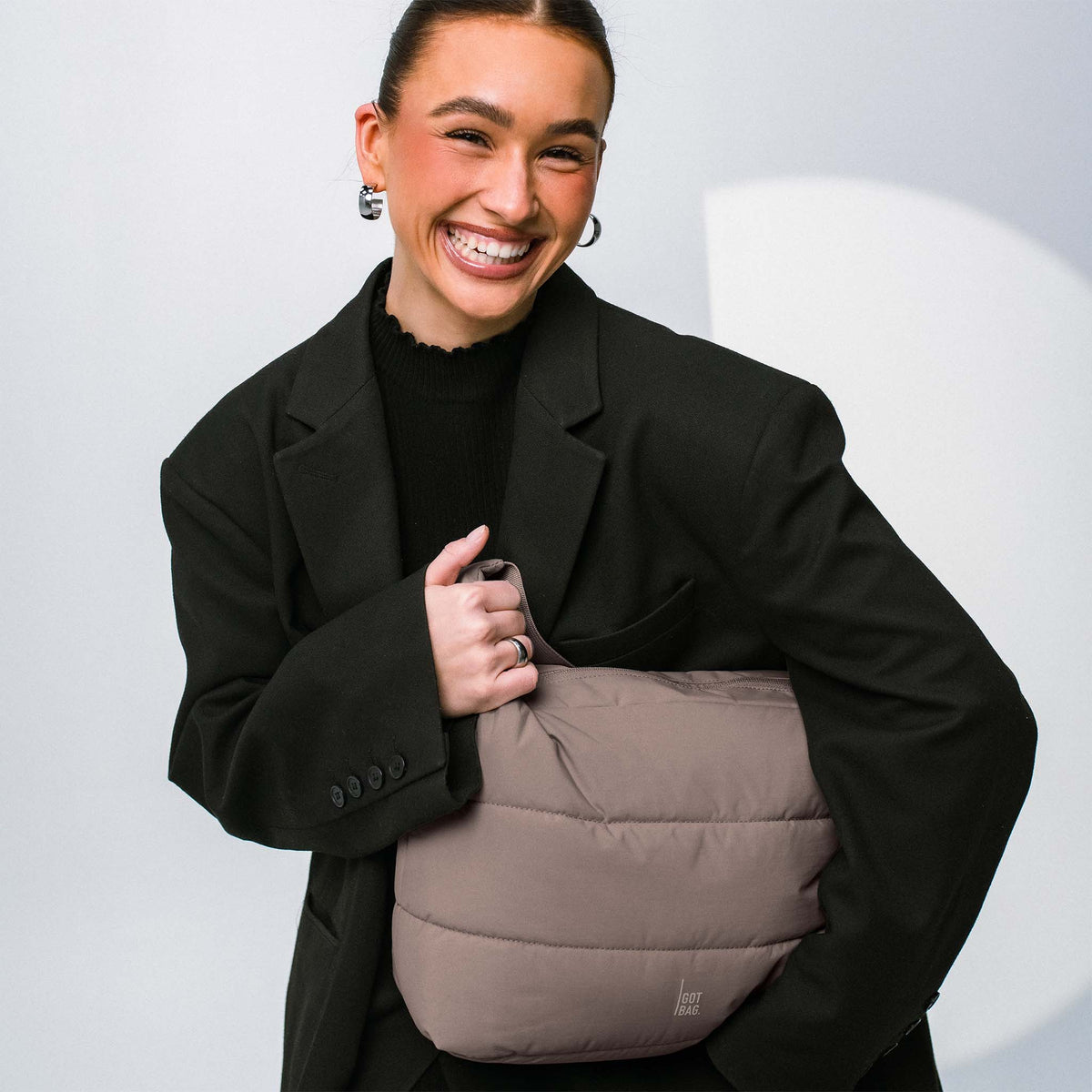 PUFFER SQUARE BAG Tasche in oyster (klassisches Taupe-Braun) von einer Frau in der Hand gehalten.