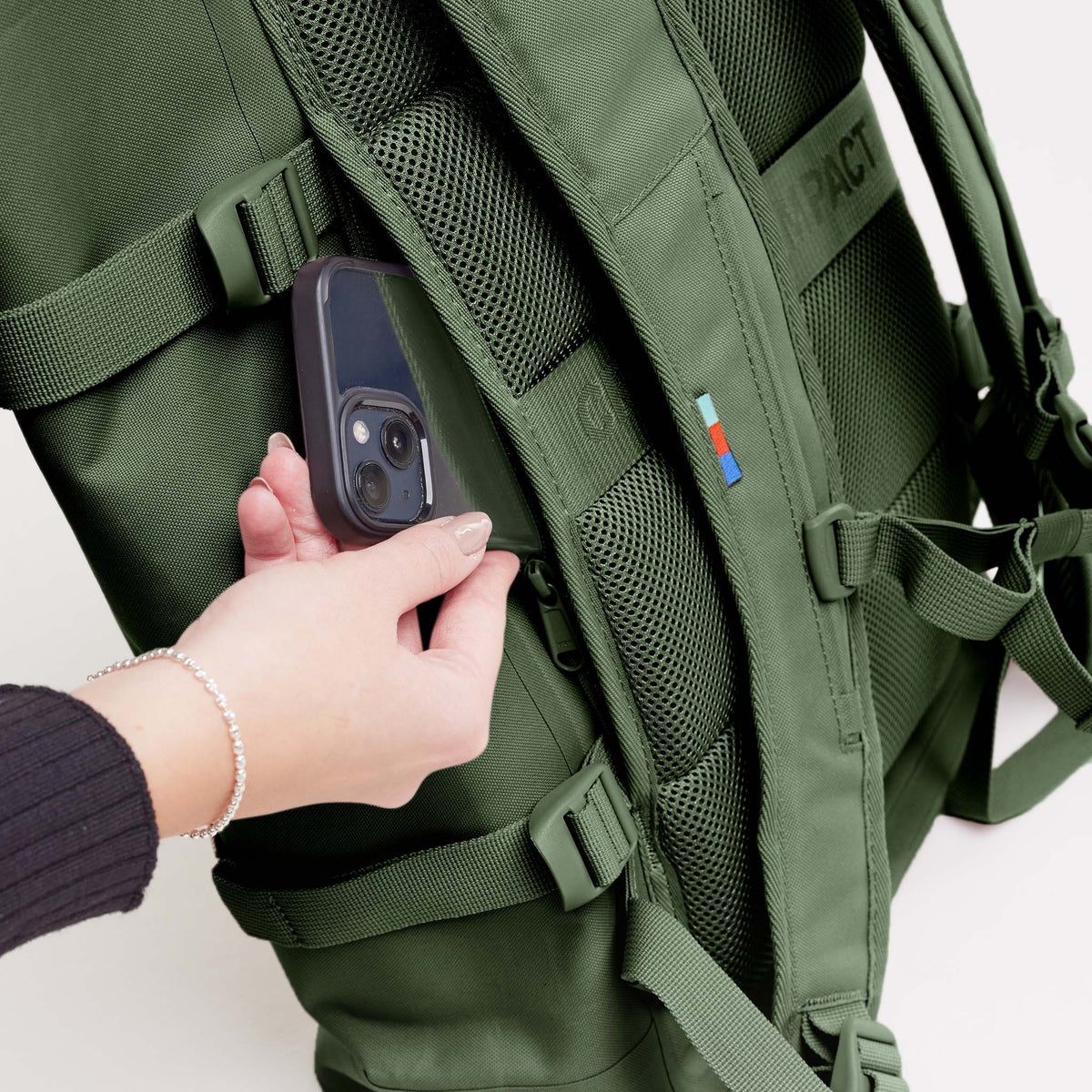 ROLLTOP 2.0 Rucksack in seafloor (tiefes Dunkelgrün) von einer Frau, die ein Handy in die Reißverschlusstasche steckt.
