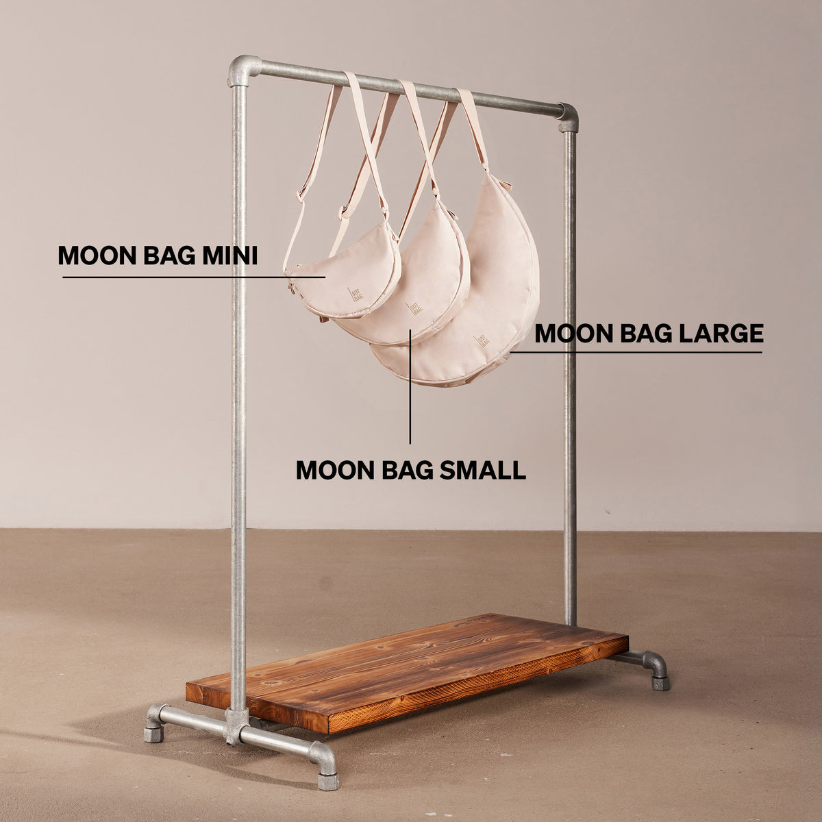 MOON BAG MINI Tasche in soft shell (warmes Cremeweiß) mit zwei weiteren MOON BAG Taschen in verschiedenen Größen auf einer Kleiderstange hängend.