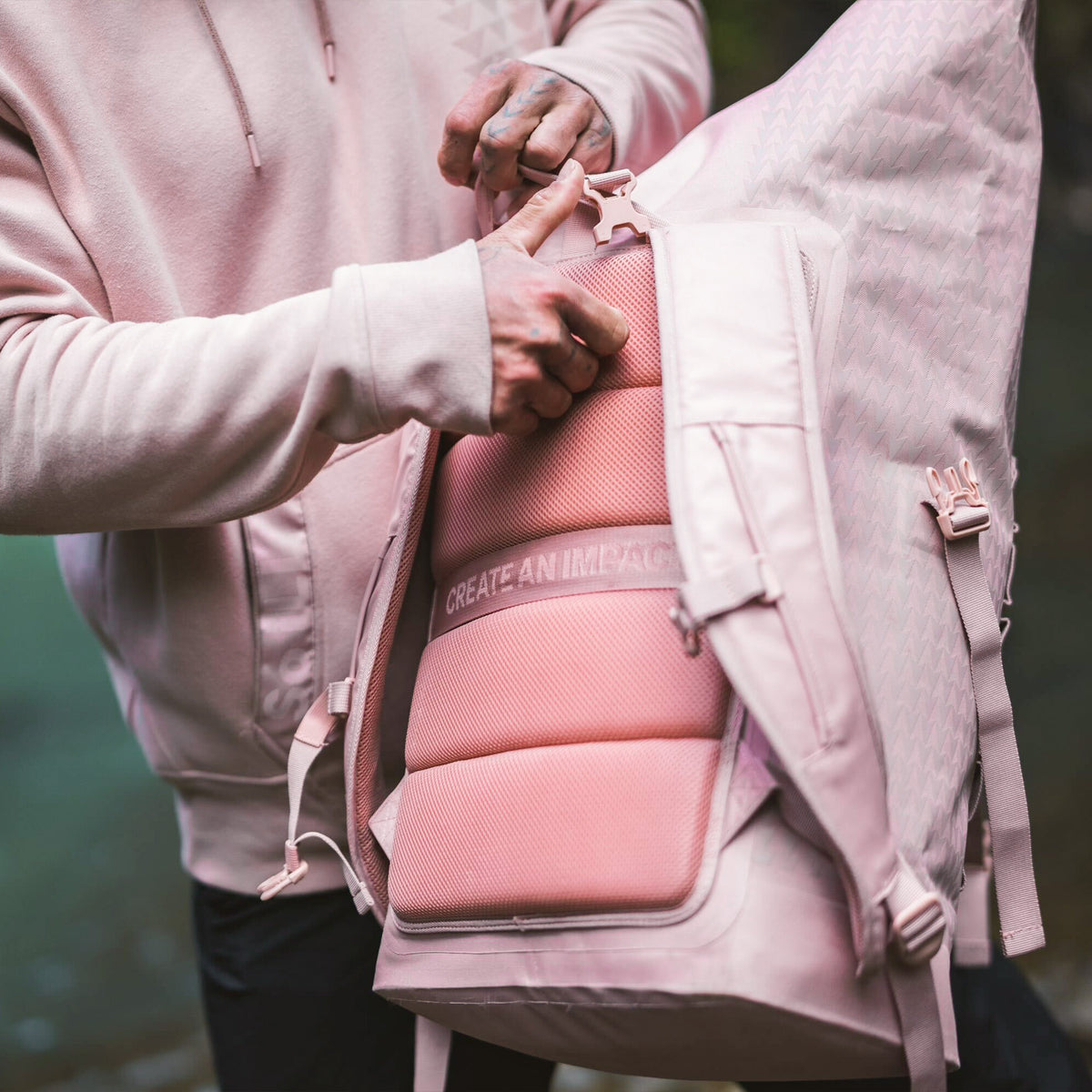 ROLLTOP ON THE ROAM Rucksack, der von einem Mann geöffnet wird und das gepolsterte Rückenteil mit CREATE AN IMPACT zeigt.