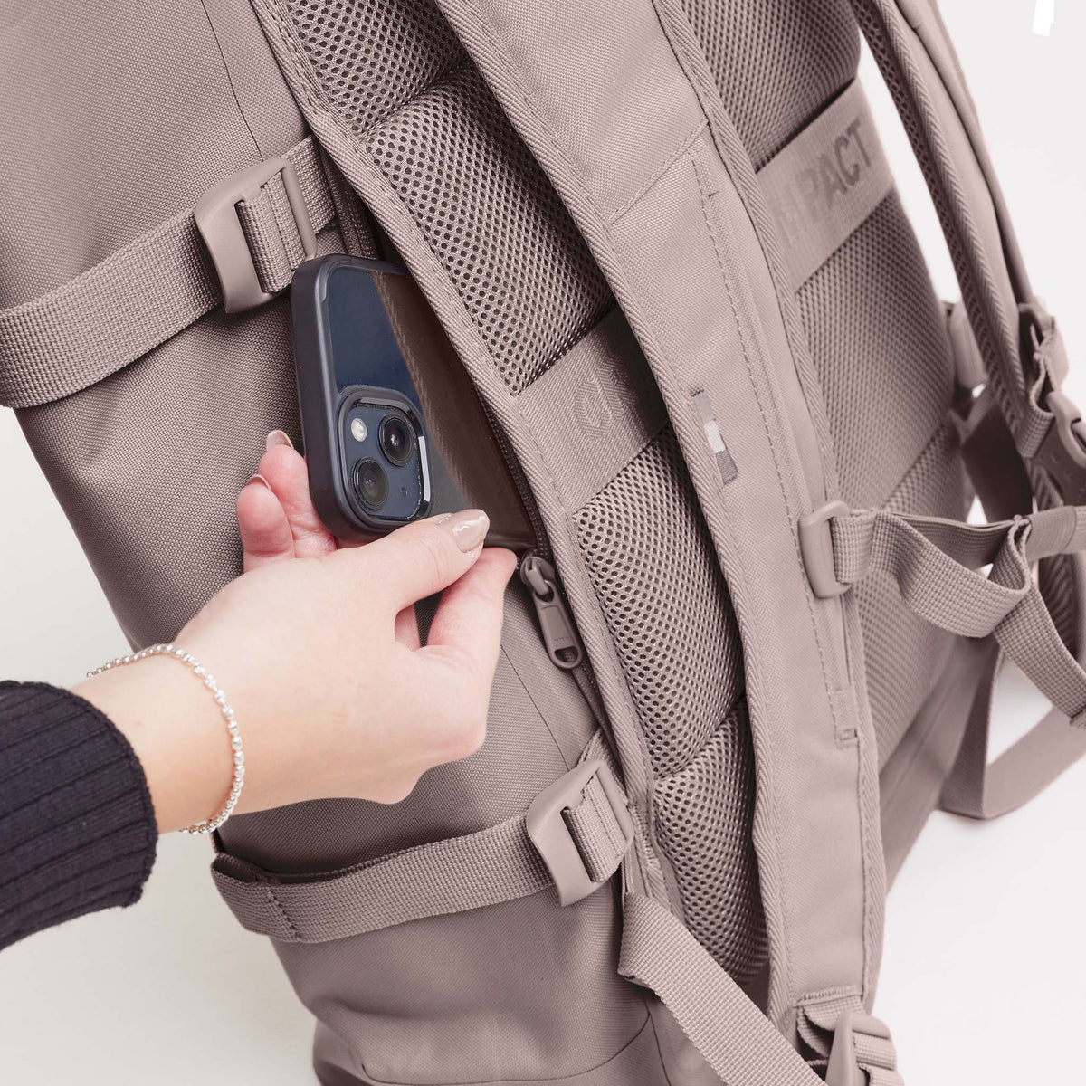 ROLLTOP Rucksack in blobfish (dunkles Altrosa), von einer Frau, die ein Smartphone in eine Reißverschlusstasche steckt.