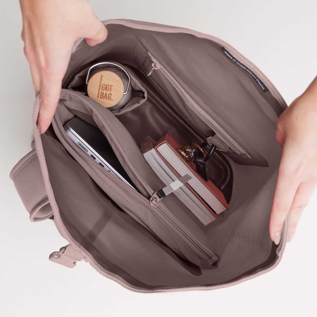 ROLLTOP LITE Tasche in blobfish (dunkles Altrosa) von Händen geöffnet, mit Blick ins Innere.