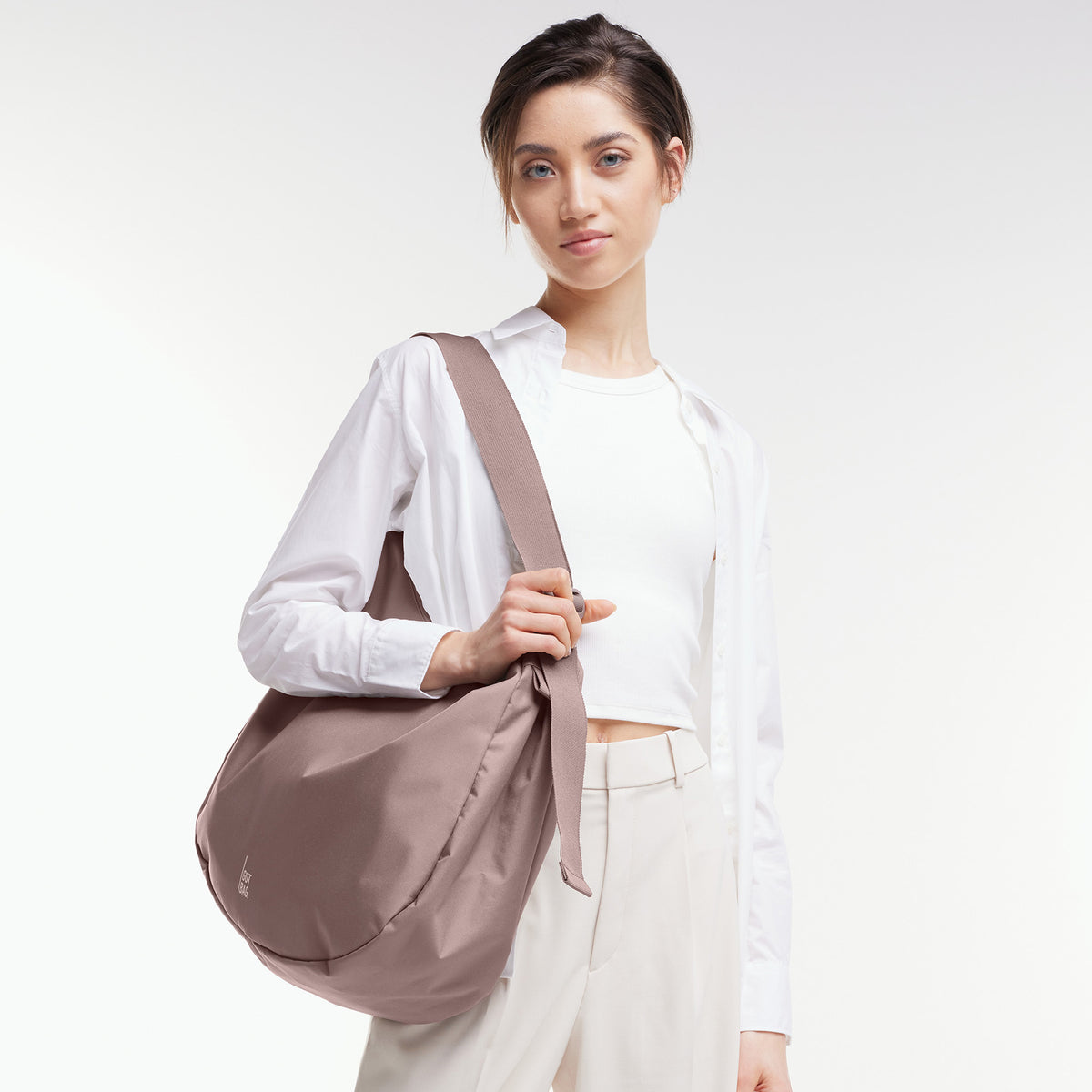 CURVED BAG Tasche in blobfish (dunkles Altrosa) von einer Frau über der Schulter getragen.