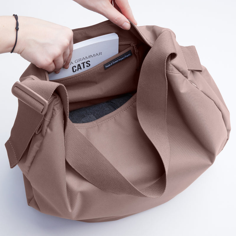 CURVED BAG MONOCHROME EDITION Tasche in blobfish (dunkles Altrosa) von einer Frau mit einem Buch in die Tasche greifend.