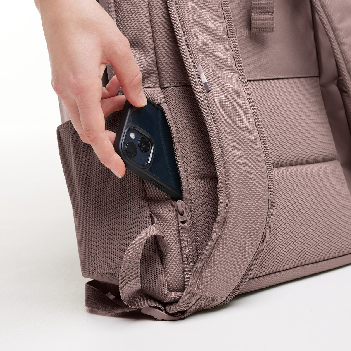 DAYPACK LOOP Rucksack. Eine Hand steckt ein Handy in die Reißverschlusstasche.
