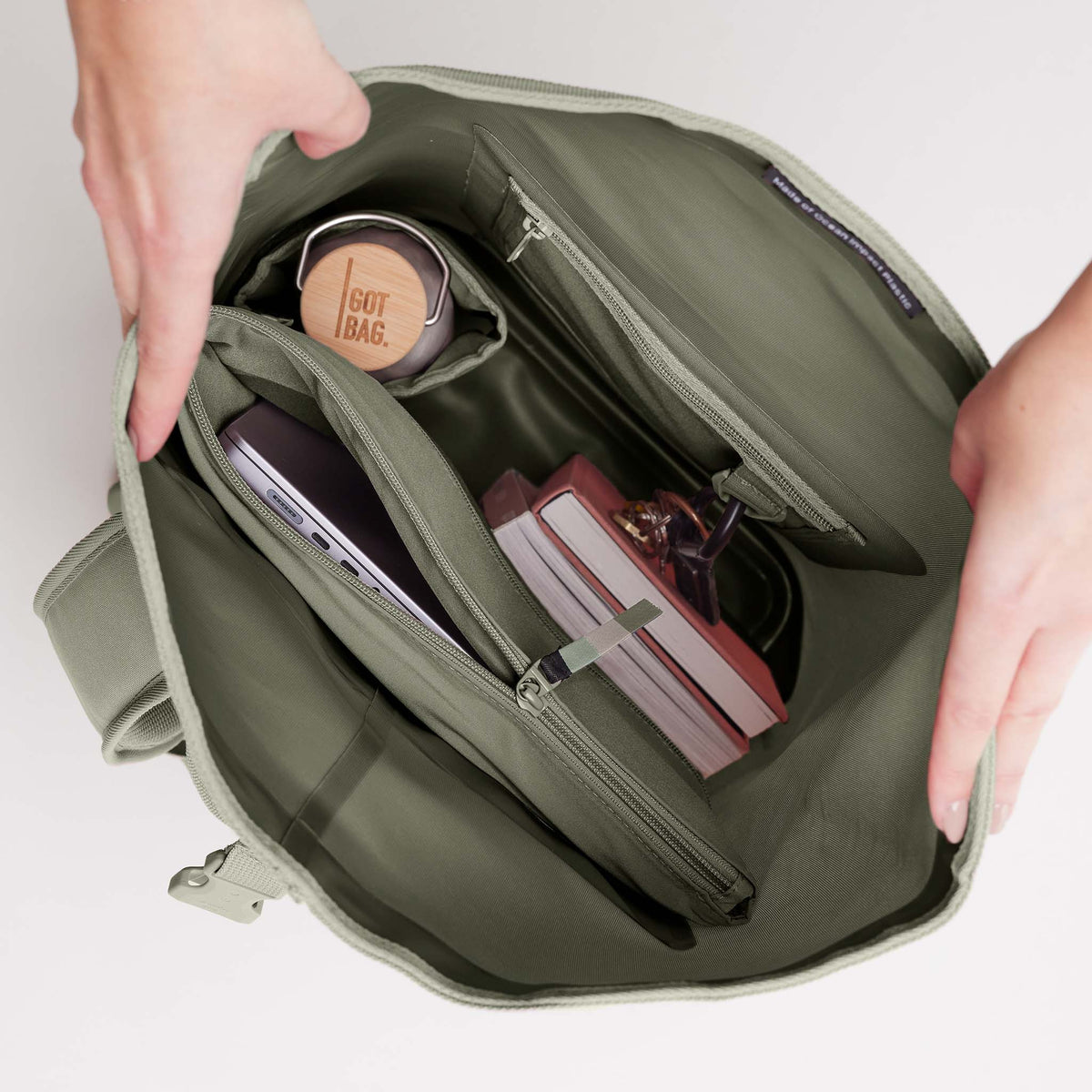 ROLLTOP 2.0 Rucksack in seabed (helles Olivgrün) geöffnet. Innen: Laptop, Flasche, Label Made of Ocean Impact Plastic.