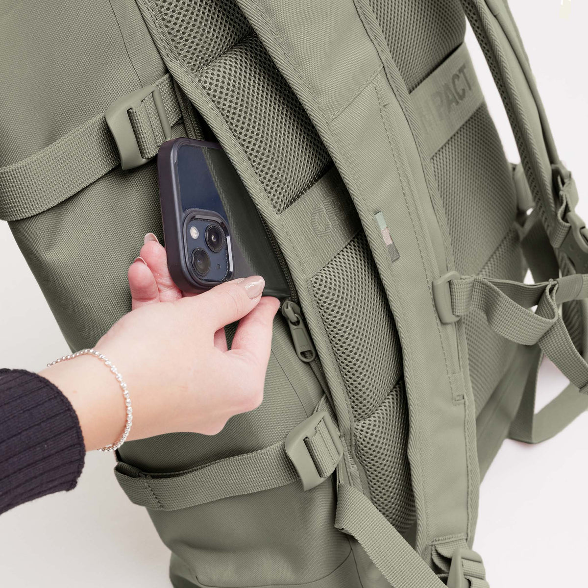 ROLLTOP 2.0 Monochrome Edition Rucksack in seabed (helles Olivgrün), von einer Frau ein Handy in die Reißverschlusstasche gesteckt.