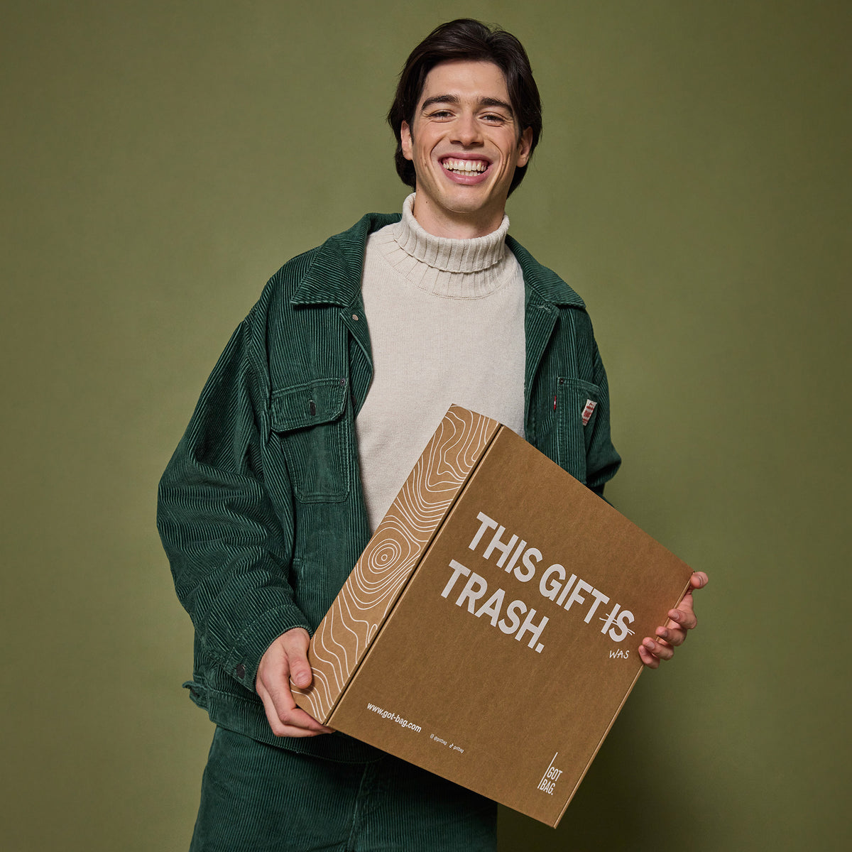 Mann hält eine braune Geschenkverpackung Accessoire mit Aufschrift THIS GIFT IS TRASH in den Händen.