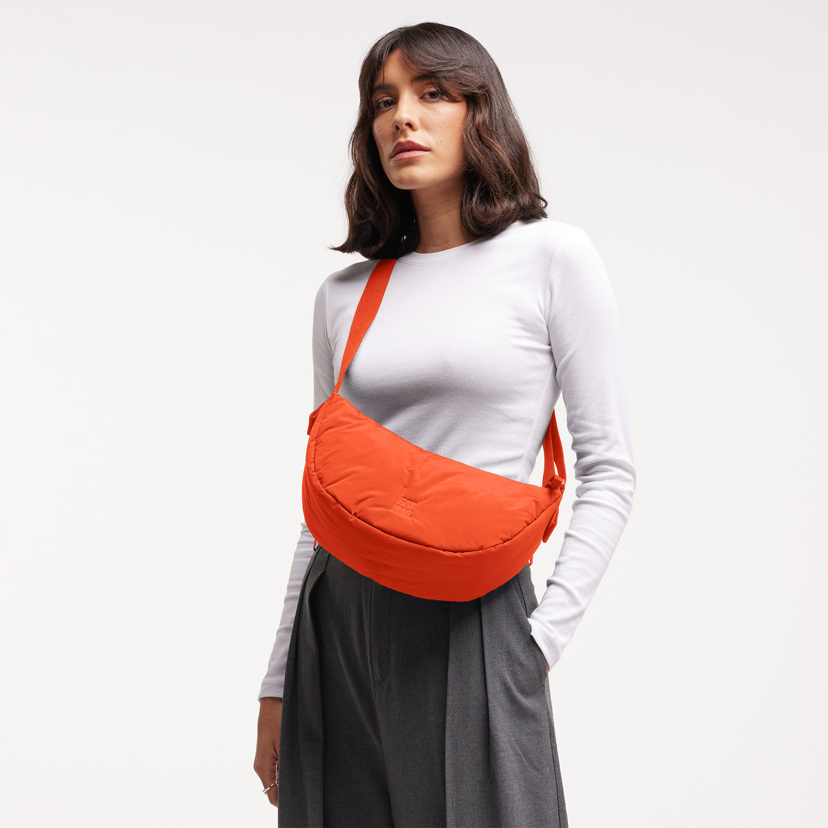 CLOUD MOON BAG SMALL Tasche in hot coral (knalliges Orange) von einer Frau crossbody getragen.