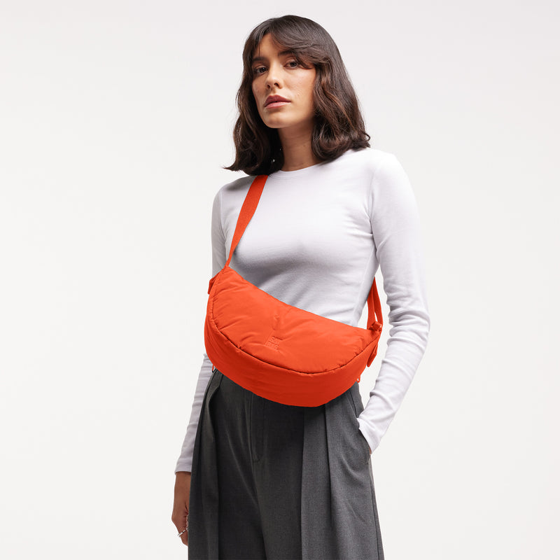 CLOUD MOON BAG SMALL Tasche in hot coral (knalliges Orange) von einer Frau crossbody getragen.