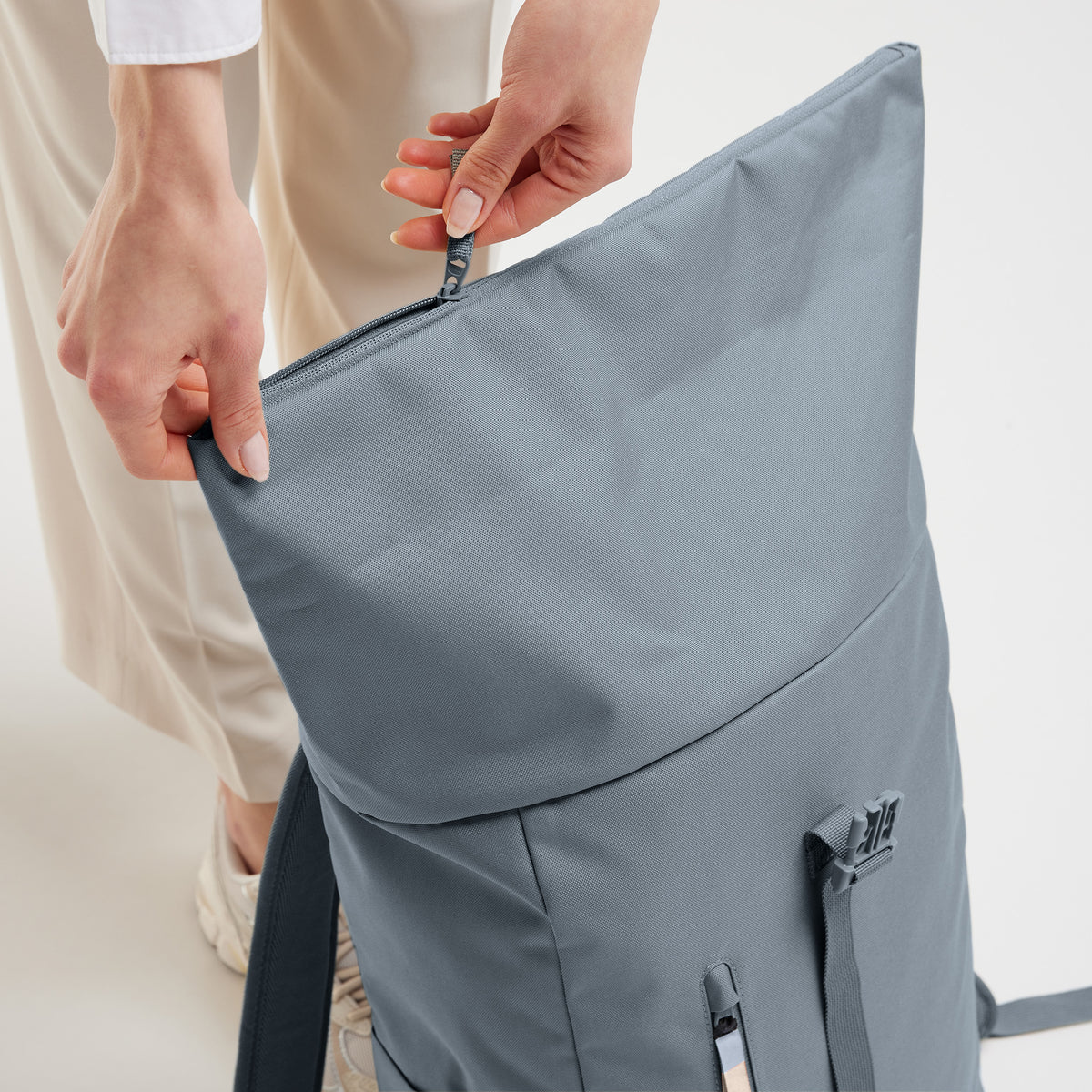 ROLLTOP EASY Rucksack in marlin (grau-blau), von einer Frau am Reißverschluss gehalten.