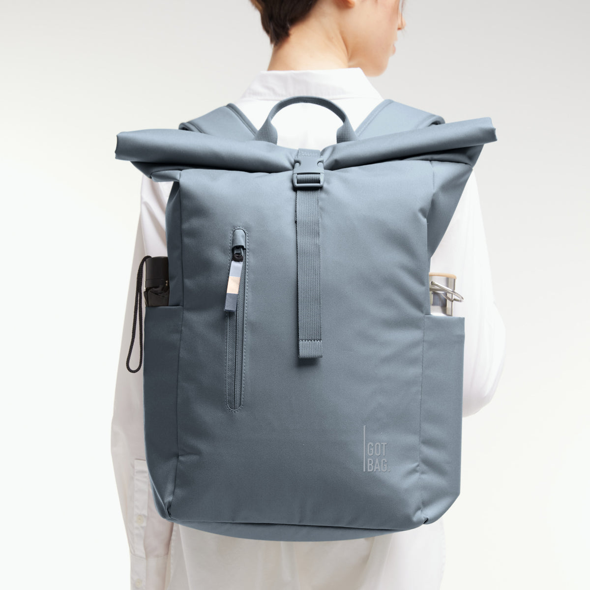 ROLLTOP EASY Rucksack in marlin (grau-blau) von einer Frau als Rucksack auf dem Rücken getragen.