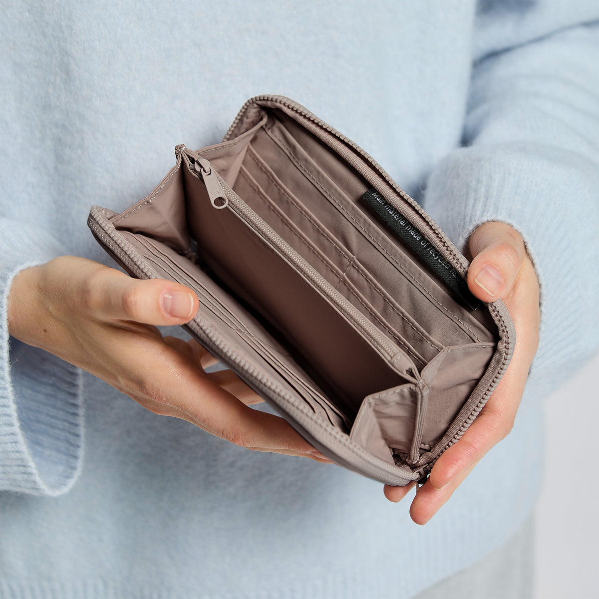 WALLET Accessoire in oyster (klassisches Taupe-Braun) von einer Frau in der Hand gehalten.