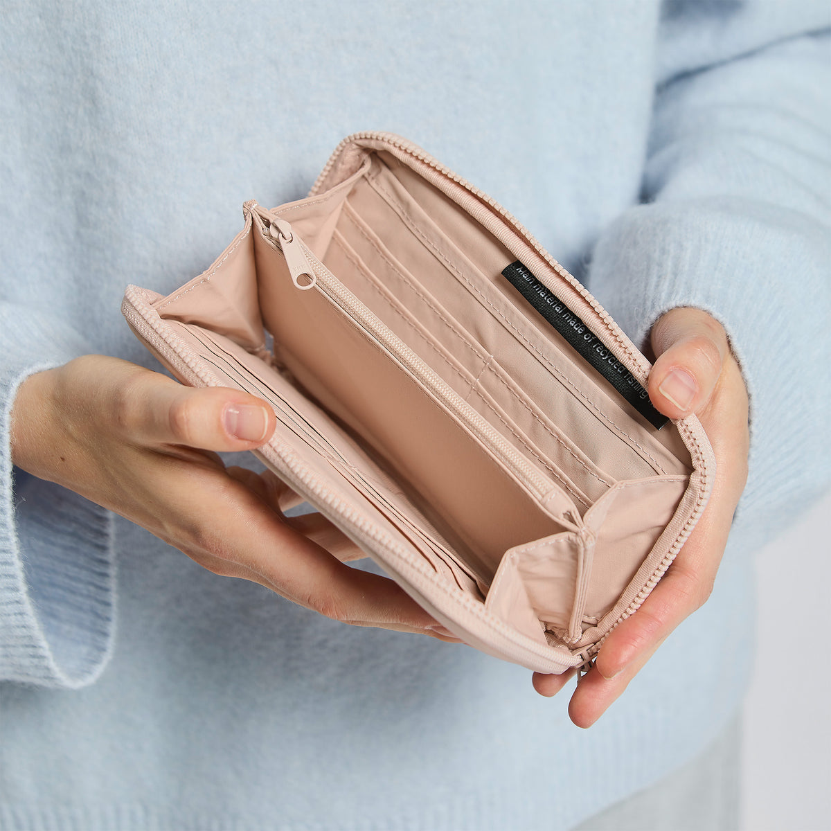 WALLET Accessoire in pearl (helles Puder-Rosa) von einer Frau in der Hand gehalten, mit Schriftzug main material made of recycled fishing im Inneren.