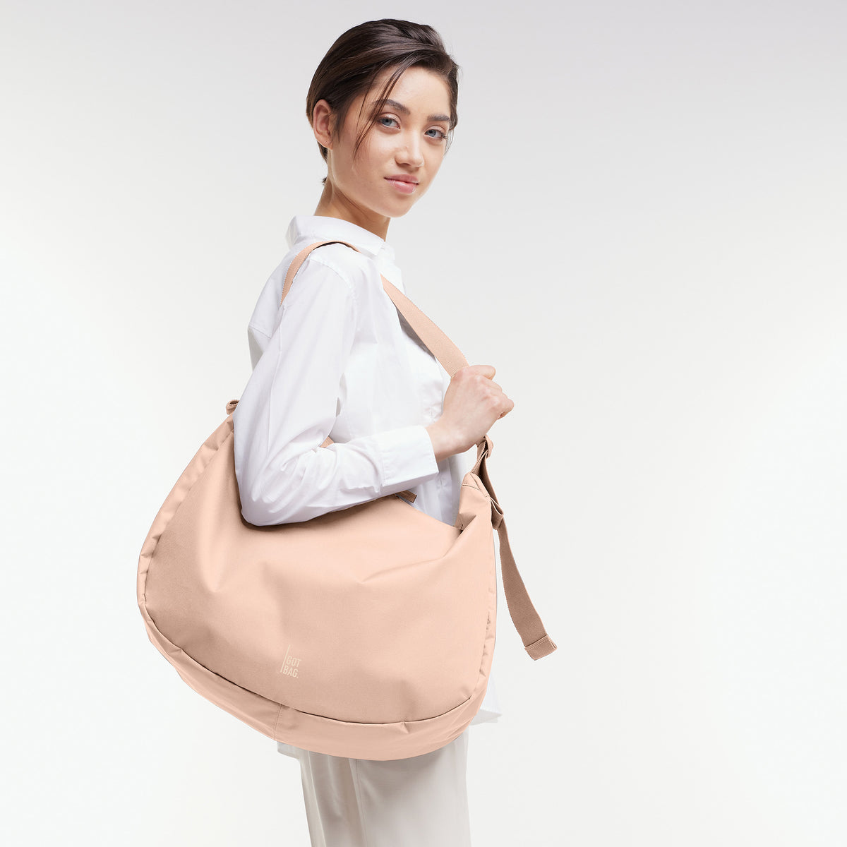 CURVED BAG Tasche in pearl (helles Puder-Rosa) von einer Frau über der Schulter getragen.