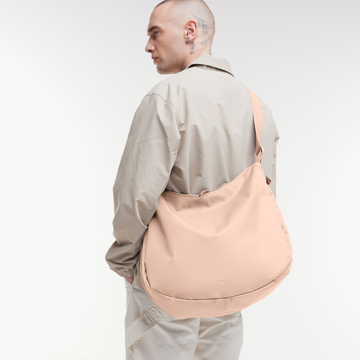 CURVED BAG Tasche in pearl (helles Puder-Rosa) von einem Mann über der Schulter getragen.