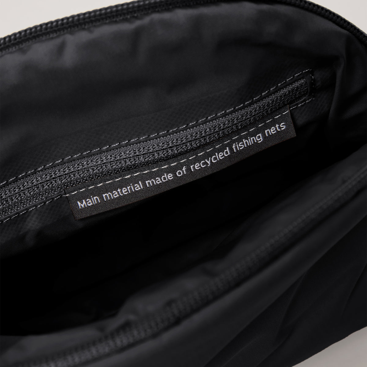 CLOUD POCKET BAG Tasche in black (Schwarz). Innenansicht mit Etikett: Main material made of recycled fishing nets.