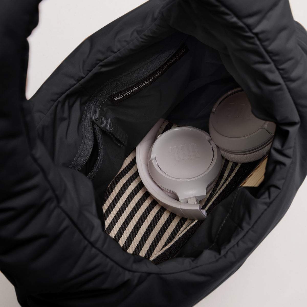 CLOUD SHOULDER Tasche in black (Schwarz) Detailaufnahme mit JBL Kopfhörern und Reißverschlussfach.