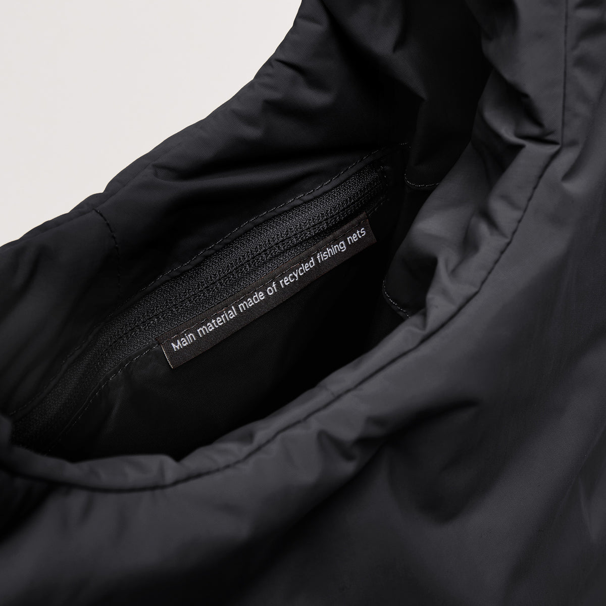 CLOUD SHOULDER Tasche in black (Schwarz). Detailaufnahme der Innenseite mit Reißverschluss und Label: Main material recycled fishing nets.