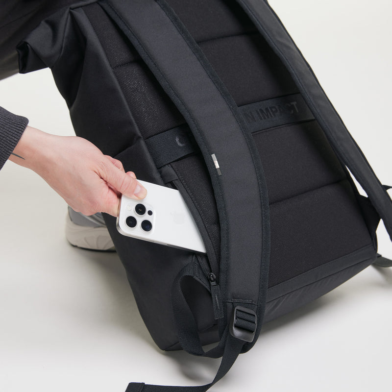 ROLLTOP EASY Rucksack in black (Schwarz) von einer Hand, die ein Smartphone in die Geheimtasche steckt.