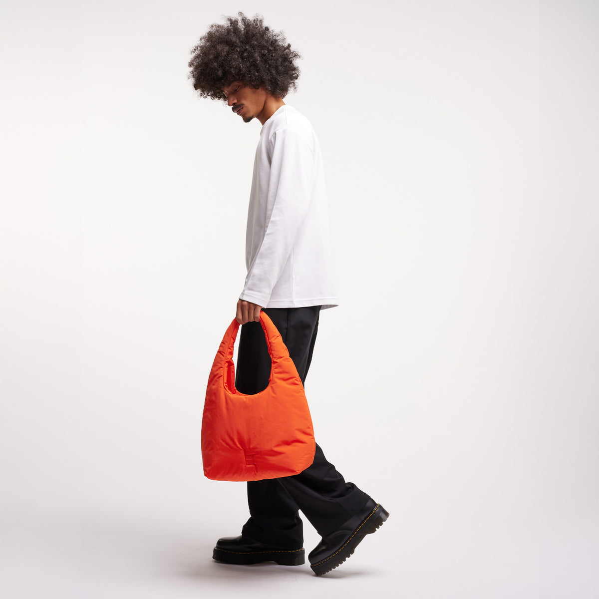CLOUD SHOULDER Tasche in hot coral (knalliges Orange) von einem Mann in der Hand gehalten.
