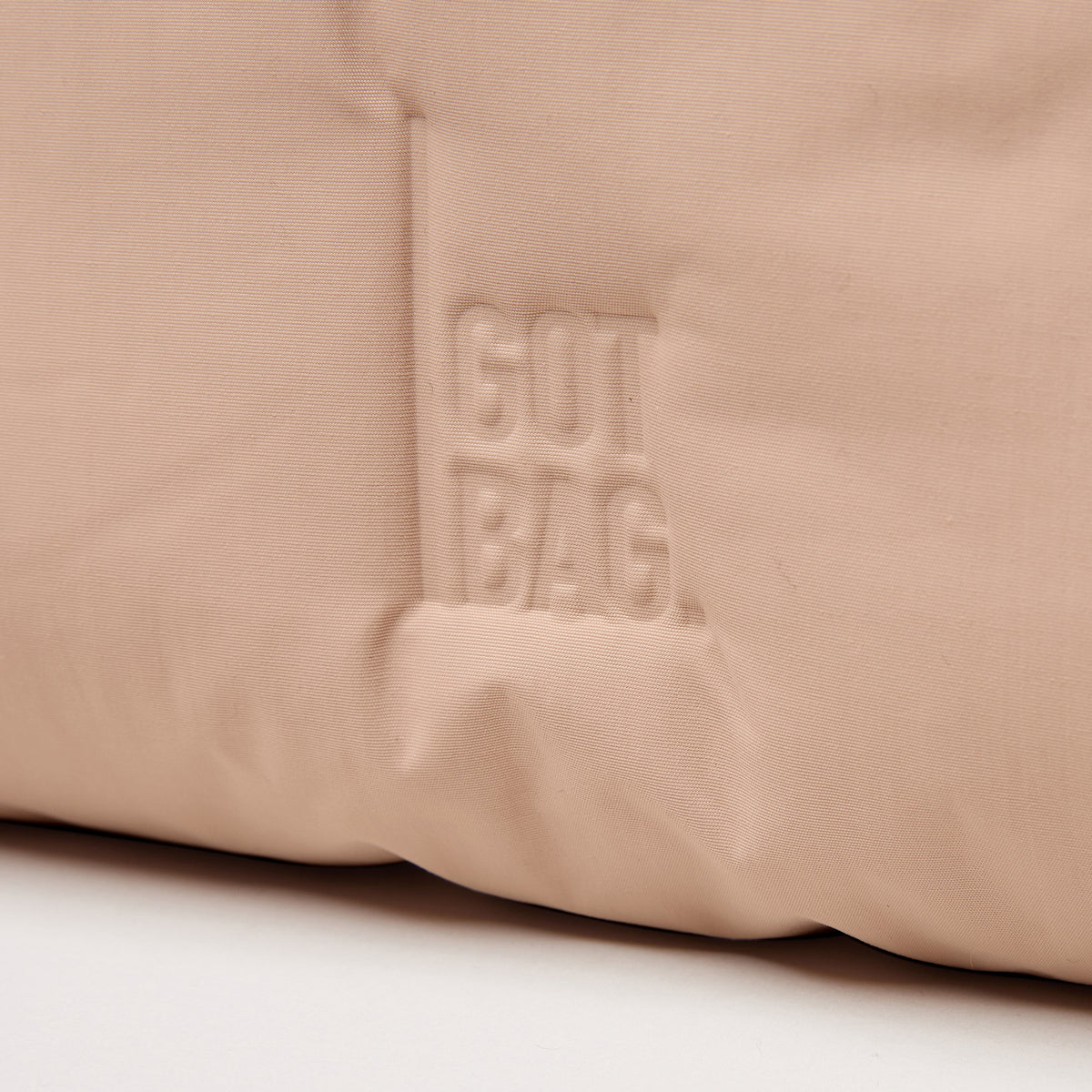 CLOUD SHOULDER Tasche in sandbar (warmes Beige mit rötlichem Unterton) mit geprägtem GUT BAG Logo als Detailaufnahme.