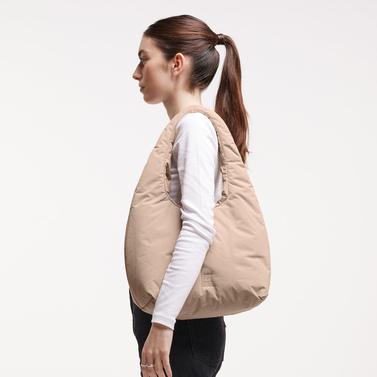 CLOUD SHOULDER Tasche in sandbar (warmes Beige mit rötlichem Unterton) von einer Frau über der Schulter getragen.