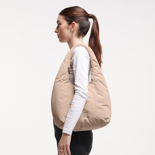 CLOUD SHOULDER Tasche in sandbar (warmes Beige mit rötlichem Unterton) von einer Frau über der Schulter getragen.