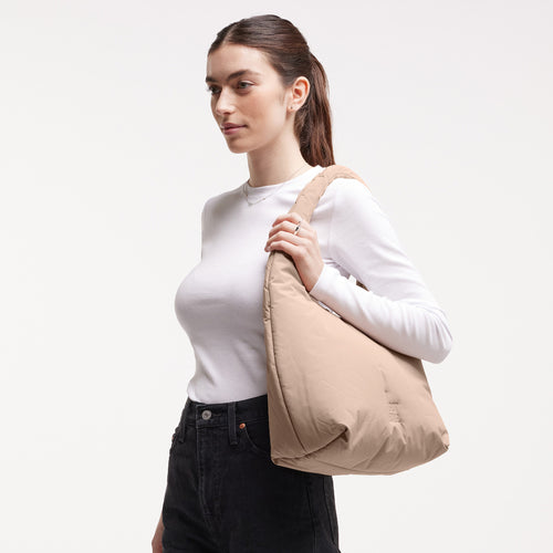 CLOUD SHOULDER Tasche in sandbar (warmes Beige mit rötlichem Unterton) von einer Frau über der Schulter getragen.