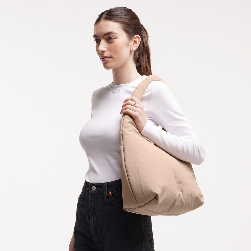 CLOUD SHOULDER Tasche in sandbar (warmes Beige mit rötlichem Unterton) von einer Frau über der Schulter getragen.