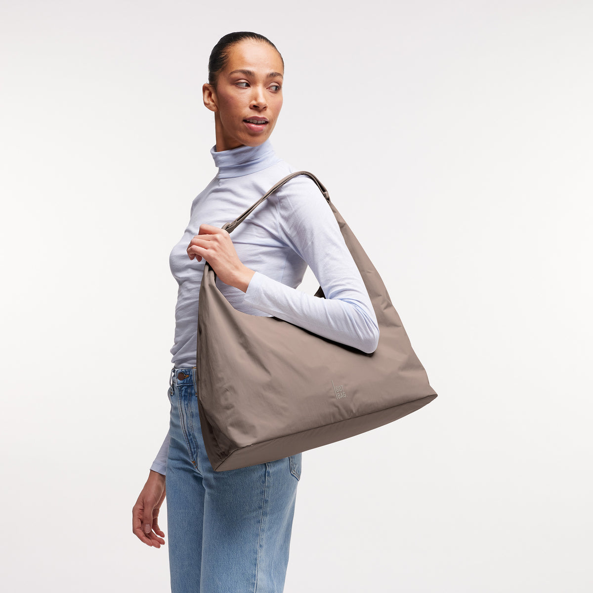T SHAPE BAG LARGE Tasche in oyster (klassisches Taupe-Braun) von einer Frau über der Schulter getragen.
