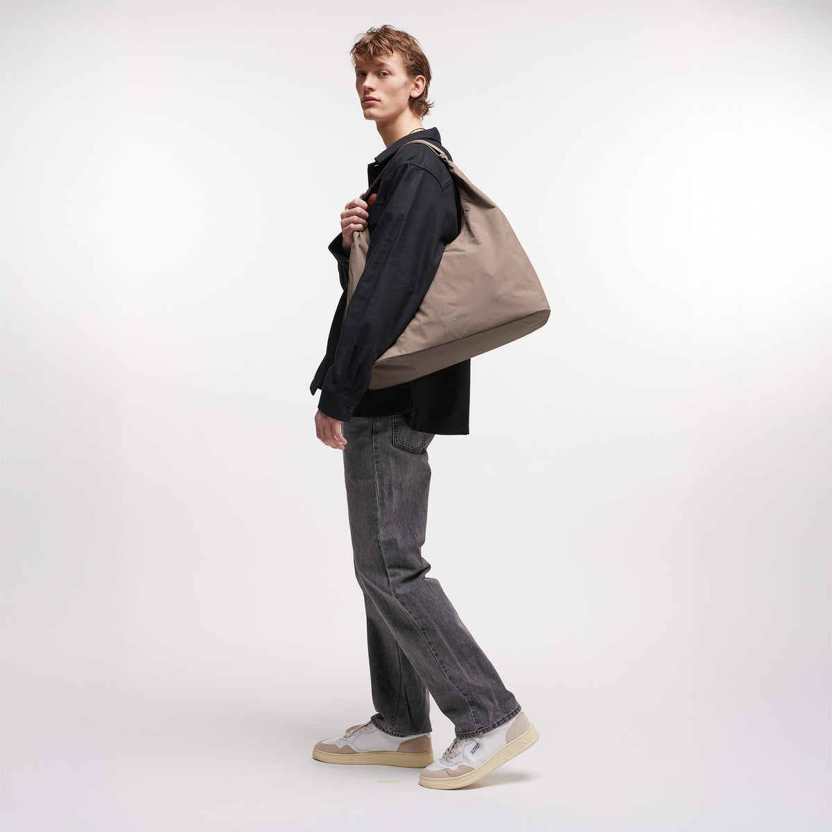 T SHAPE LARGE Tasche in oyster (klassisches Taupe-Braun) von einem Mann über der Schulter getragen.