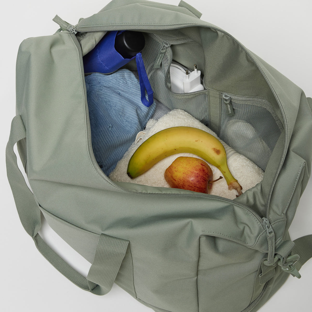 WEEKEND BAG Tasche in bass (Salbeigrün) in Innenansicht mit Regenschirm, Ladegerät, Banane und Apfel.