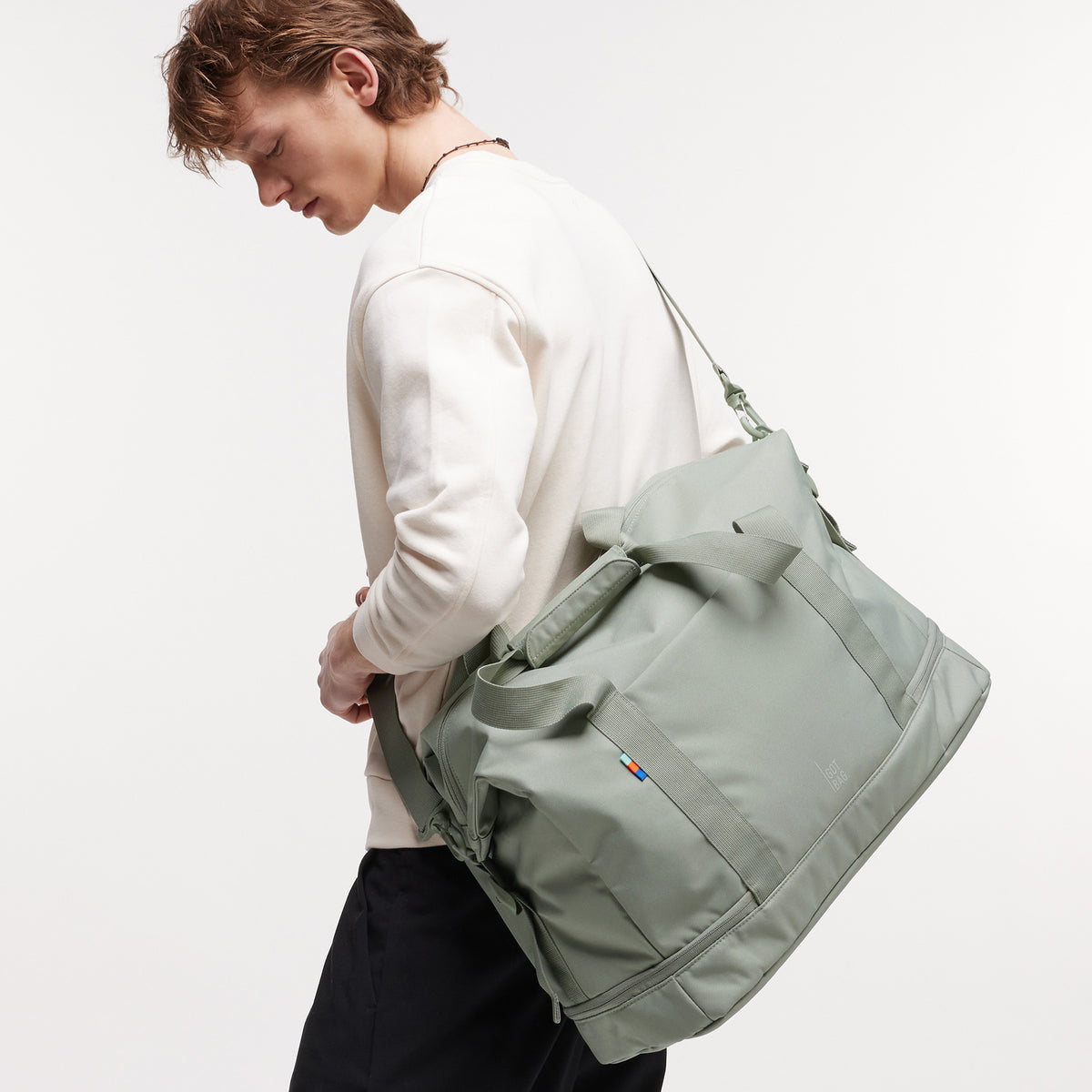 WEEKEND BAG Tasche in bass (Salbeigrün) von einem Mann über der Schulter getragen.