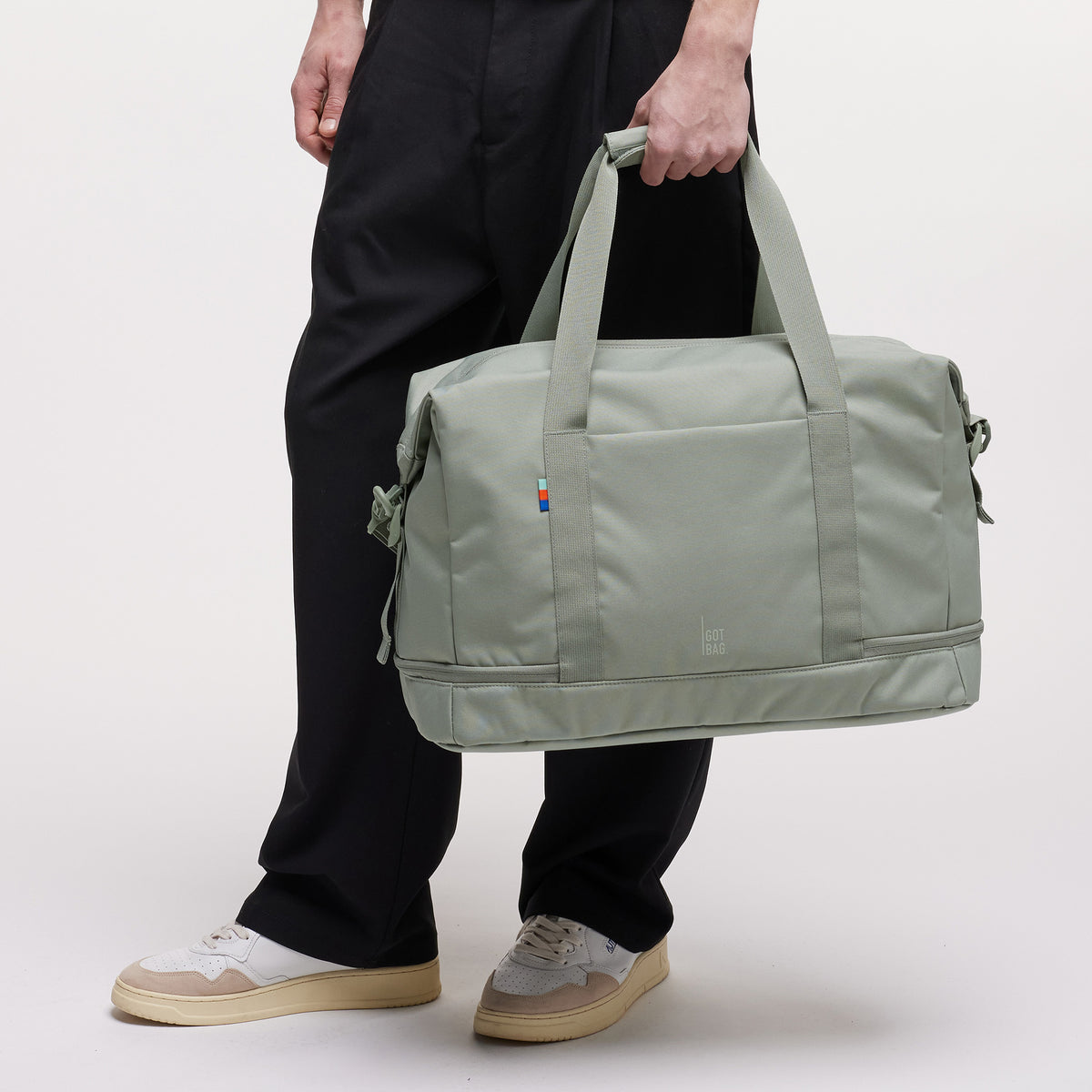 WEEKEND BAG Tasche in bass (Salbeigrün) von einem Mann in der Hand gehalten.