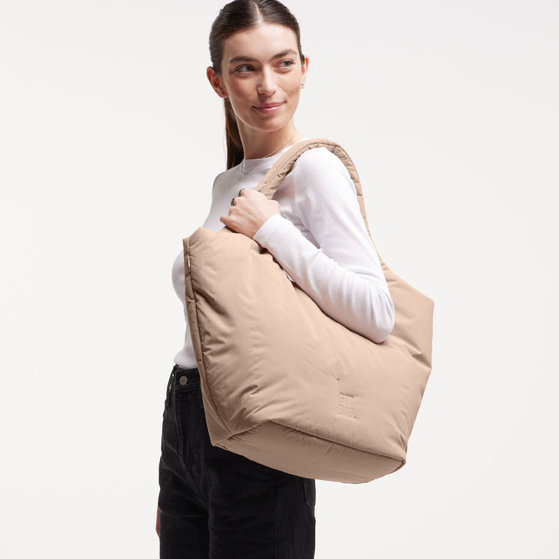 CLOUD TOTE BAG Tasche in sandbar (warmes Beige mit rötlichem Unterton) von einer Frau über der Schulter getragen.