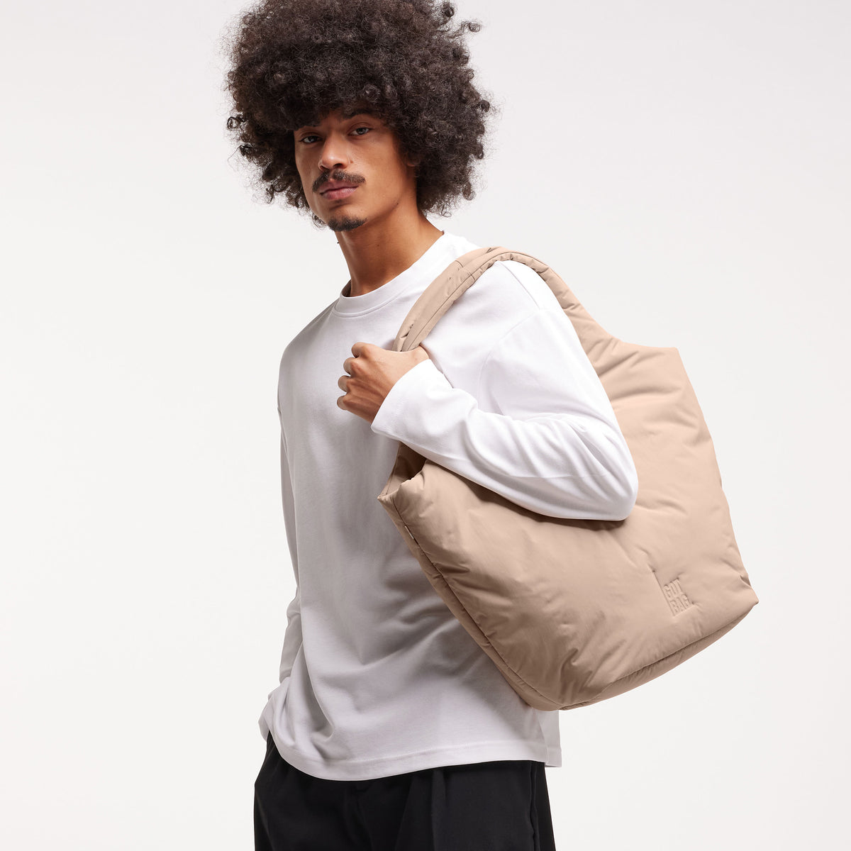 CLOUD TOTE BAG Tasche in sandbar (warmes Beige mit rötlichem Unterton) von einem Mann über der Schulter getragen.