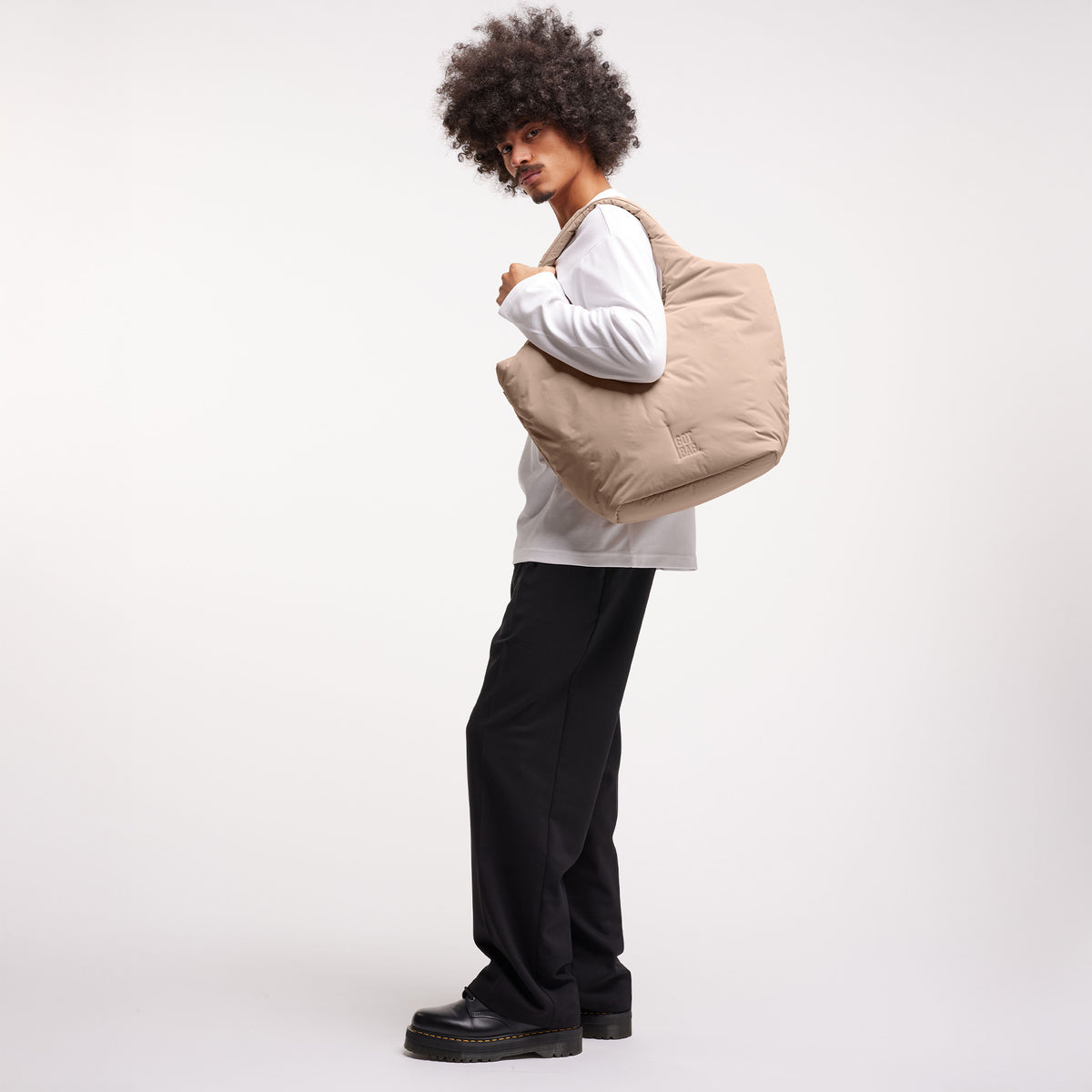 CLOUD TOTE BAG Tasche in sandbar (warmes Beige mit rötlichem Unterton) von einem Mann über der Schulter getragen.
